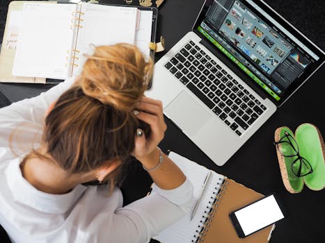 pexels-photo-313690-313690 Overhead view of a stressed woman working at a desk with a laptop, phone, and notebooks.
